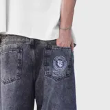 Jean de corte ultra baggy con efecto lavado ácido en color negro. Presenta un diseño holgado, bolsillos traseros amplios y un estampado gráfico circular en el bolsillo derecho.