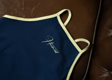 Musculosa deportiva de lycra color azul marino con ribetes y tirantes finos en color amarillo claro. Presenta un logo caligráfico en color amarillo claro en el pecho.