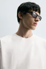 Camiseta blanca de corte holgado, cuello redondo y manga corta. Presenta un parche bordado en la espalda con diseño a contraste.