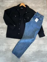 Chaqueta negra de paño con cuello clásico, cierre frontal con botones a presión, dos bolsillos de parche en el pecho y corte holgado.