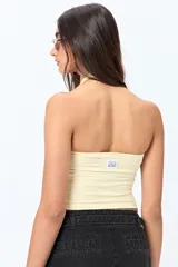 Top halter color marrón, con escote redondeado y detalle de ojales metálicos a lo largo del cuello. Presenta un diseño ajustado al cuerpo y espalda descubierta.