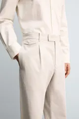 Pantalón de corte relajado confeccionado en tejido de algodón con estructura twill. Presenta pliegues frontales, bolsillos laterales y bolsillos traseros de doble vivo con botón. Cierre frontal con cremallera y botón.