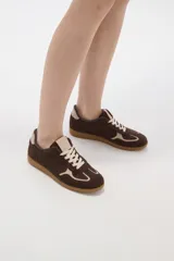 Zapatilla urbana de gamuza color marrón con detalles en beige, cordones claros y suela de goma tipo caramelo.