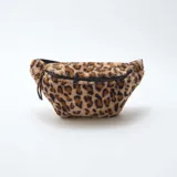 Riñonera de textura suave tipo peluche con estampado animal print de leopardo. Cuenta con cierre superior negro y correa ajustable.