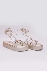 Sandalias de plataforma color dorado con tiras plateadas y cobrizas para atar alrededor del tobillo.