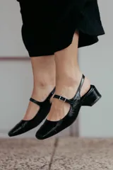 Zapato estilo Mary Jane con diseño destalonado, confeccionado en cuero color beige. Presenta una tira fina con hebilla metálica sobre el empeine, punta redondeada y taco cuadrado forrado de 6 cm de altura.