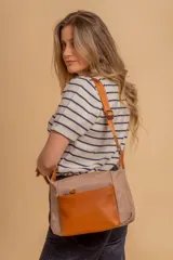 Bandolera de diseño moderno confeccionada en tela color beige con bolsillo frontal y detalles en cuero sintético color suela. Cuenta con correa regulable y cierre principal.