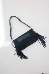 Cartera bandolera de cuero negro con flecos colgantes en los laterales y detalle de aplique de cuero texturado en la solapa. Cuenta con una correa larga ajustable.