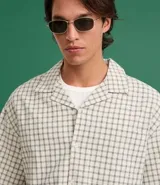 Camisa de hombre de manga corta, cuello inglés y corte boxy, confeccionada en algodón tricolina texturizada a cuadros. Presenta abotonado frontal y bordado en la espalda.