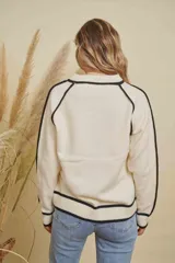 Buzo de tejido de punto en color blanco crema, con cuello redondo y detalles de líneas horizontales en color negro en el cuello, puños, ruedo y a lo largo de las mangas.