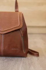 Mochila de cuero vacuno marrón con acabado pulido, solapa en forma de V y costuras decorativas. Cuenta con cremalleras laterales y asas ajustables.