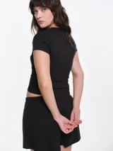 Remera de manga corta entallada en tejido pointelle, con escote redondo y detalle de picot con lazo pequeño en el centro. Diseño ajustado al cuerpo con textura acanalada.