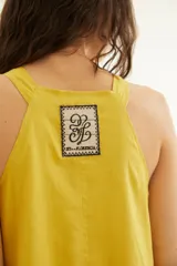 Vestido largo de lino color amarillo mostaza, sin mangas con diseño de espalda nadadora y escote a la base, con detalles de mini volados horizontales escalonados a lo largo de la falda.