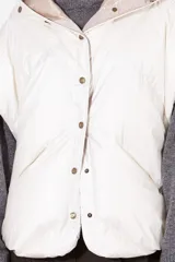 Campera tipo capa acolchada, con capucha y cierre frontal de botones a presión. El exterior es de nylon color beige claro metalizado y el forro de la capucha es verde militar.