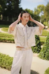 Camisa corta de lino color blanco, con cuello clásico, mangas cortas y detalles bordados florales en la parte delantera y las mangas.