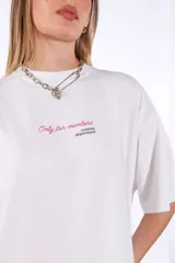 Remera de algodón blanca, corte oversize, con cuello redondo y manga corta. Presenta un pequeño estampado centrado en el pecho con texto en cursiva.
