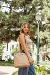 Bandolera negra de cuero sintético con dos bolsillos frontales, cierre metálico y dos correas intercambiables: una de cuero sintético y otra de tela con rayas rosas y negras.