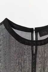 Top combinado de punto color negro, con cuello redondo, manga corta y detalles semitransparentes en la parte superior. Cuenta con costura central marcada en el frente y cierre en la espalda con abertura y botón.