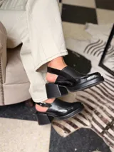 Zapato tipo slingback color negro, con plataforma y taco cuadrado. Presenta una puntera cuadrada y cierre con hebilla metálica en la tira trasera.