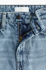 Jean tobillero de denim de algodón rígido, de tiro alto y diseño curvo con volumen en las piernas. Presenta cinco bolsillos, cierre de cremallera y botón, pinzas en las rodillas y costuras laterales avanzadas.