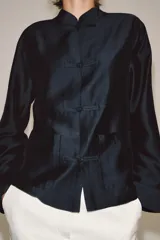 Camisa de estilo oriental confeccionada en mezcla de lyocell con acabado satinado. Presenta cuello redondo, manga larga con puños rectos, bolsillos de plastrón y cierre frontal mediante alamares.