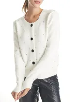 Cardigan de punto color blanco con cuello redondo, manga larga y cierre frontal con botones forrados en terciopelo negro. Presenta un diseño de textura acolchada con apliques de strass distribuidos por toda la prenda.