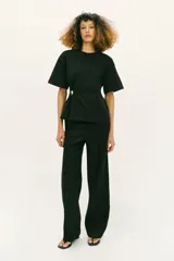 Camiseta de algodón compacto color negro, con cuello redondo, manga corta y detalle de aplique metálico en el frente que genera un ligero fruncido lateral.