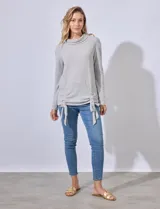 Buzo gris de tejido labrado, con cuello volcado y ruedo con terminaciones fruncidas regulables con lazo.