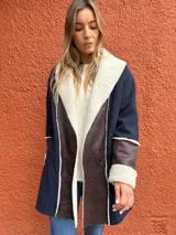 Saco de paño azul marino con solapas amplias y puños en corderito sintético color crema. Presenta detalles en cuero sintético marrón en la parte frontal y en las mangas, con un diseño abierto y corte recto.