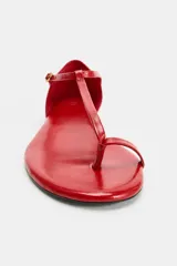 Sandalia plana de piel en color rojo, con diseño de tiras tipo thong que incluye posición para el dedo, cierre mediante hebilla metálica en el tobillo y suela fina.