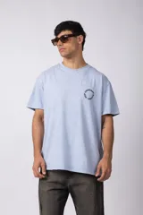 Remera de corte oversize con efecto lavado gastado, color celeste. Presenta un estampado circular con el texto VCP CONCEPT STUDIO en el pecho y en la espalda.