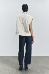 Chaleco gris acolchado con cuello alto, cierre frontal con cremallera metálica, bolsillos de plastrón en delantero y bajo ajustable con cordones.