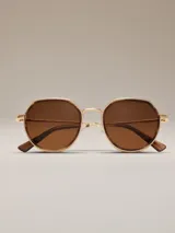 Lentes de sol con marco metálico en tono bronce y forma geométrica hexagonal. Poseen cristales en color marrón degradado y puente nasal doble.