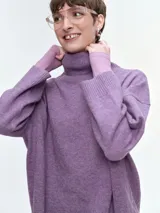 Buzo de tejido de punto color violeta, con cuello alto acanalado, hombros caídos y diseño holgado. Presenta puños y ruedo con terminación acanalada.
