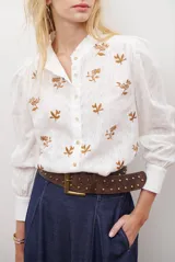 Camisa blanca de manga corta con cuello mao y volados, botones frontales y bordados de hojas y flores en color dorado.
