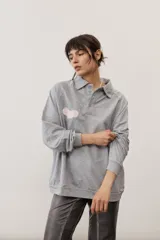 Buzo celeste de manga larga con cuello polo y cierre frontal de botones. Presenta un parche marrón bordado en el pecho.