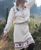 Cardigan tejido de punto color marfil, con bordados artesanales florales y paisley, cierre frontal de botones y detalles de costuras a contratono.