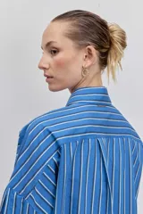 Camisa de corte oversize con diseño de rayas verticales en tonos azul y blanco, cuello clásico, cierre frontal con botones y mangas largas con puños abotonados.