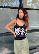 Musculosa color negro con tirantes finos y escote redondo. Presenta un diseño tridimensional en el frente realizado con tela fruncida blanca.