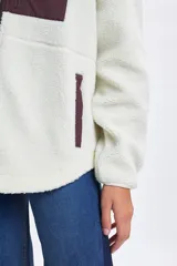 Campera de sherpa color crudo con cuello alto, cierre frontal completo y detalles en color bordó. Presenta un bolsillo frontal con cierre y dos bolsillos laterales, todos con terminaciones en contraste.