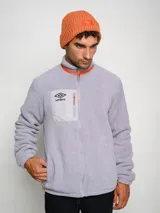 Gorro tipo beanie de tejido acanalado en color azul, con parche rectangular rojo en el frente que presenta el logo de la marca Umbro bordado en blanco.