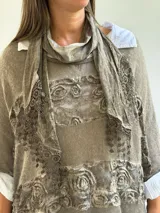 Sweater de punto color visón con diseño superpuesto, que incluye una bufanda integrada y detalles de encaje floral en el frente. Presenta mangas tres cuartos con puños abotonados y un corte holgado.