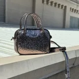 Bolso de mano Adidas Adicolor tamaño XS, con acabado metalizado texturizado y logo del trébol en el frente. Incluye doble asa superior y correa ajustable extraíble.