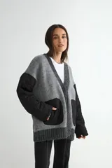 Saco tipo cardigan de punto gris con diseño híbrido. Presenta mangas largas y bolsillos frontales de tela técnica acolchada en color negro, con cierre frontal de botones y bordes acanalados.
