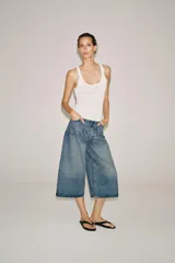 Bermuda de denim de tiro medio y corte wide leg, con diseño culotte, trabillas en la cintura y pliegues delanteros. Posee cinco bolsillos y cierre frontal con cremallera y botón.