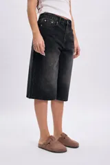 Bermuda de jean negro con efecto acid wash y diseño amplio de corte bermuda, con bolsillos laterales y traseros, y cierre frontal con botón y cremallera.