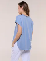 Remera de silueta amplia y relajada confeccionada en algodón y poliéster, de color verde, con escote a la base y mangas cortas de hombro caído. Presenta dobladillo enrollado y ruedo curvo.