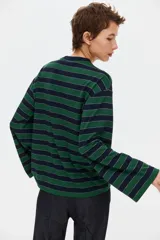 Remera de punto a rayas horizontales en color verde y azul marino, con cuello redondo, mangas largas de hombros caídos y un bolsillo de parche en el pecho.