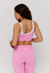 Conjunto deportivo compuesto por un top y un pantalón largo. El top es de estilo deportivo con breteles blancos y logo estampado en el frente. El pantalón es de tiro alto, corte ajustado en la parte superior y ligeramente acampanado en el ruedo, con costuras decorativas laterales.