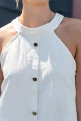 Vestido corto de color beige con cuello halter, diseño sin mangas y cierre frontal con botones dorados.